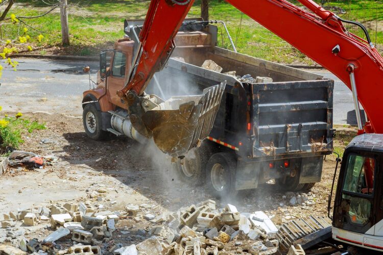 Excavator dumping demolition debris into a truck for waste management at a construction site.